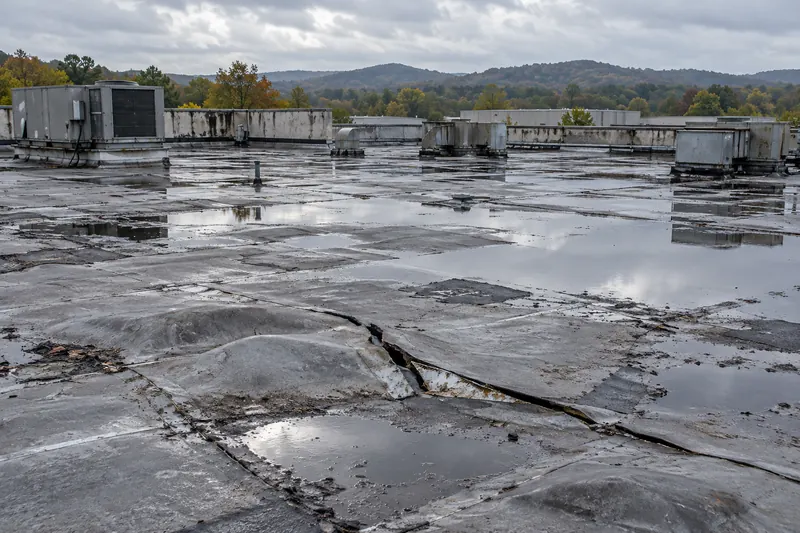Aged flat roof with ponding water, blistered membrane, and split seams