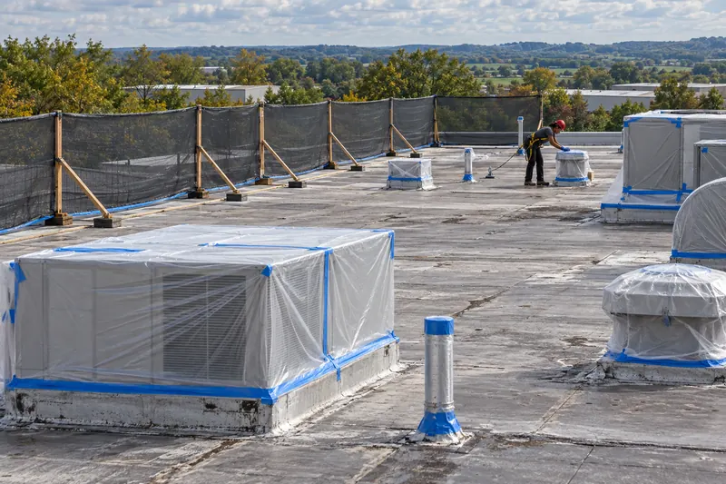 Rooftop units and vents wrapped in plastic and tape behind a braced wind screen before spraying